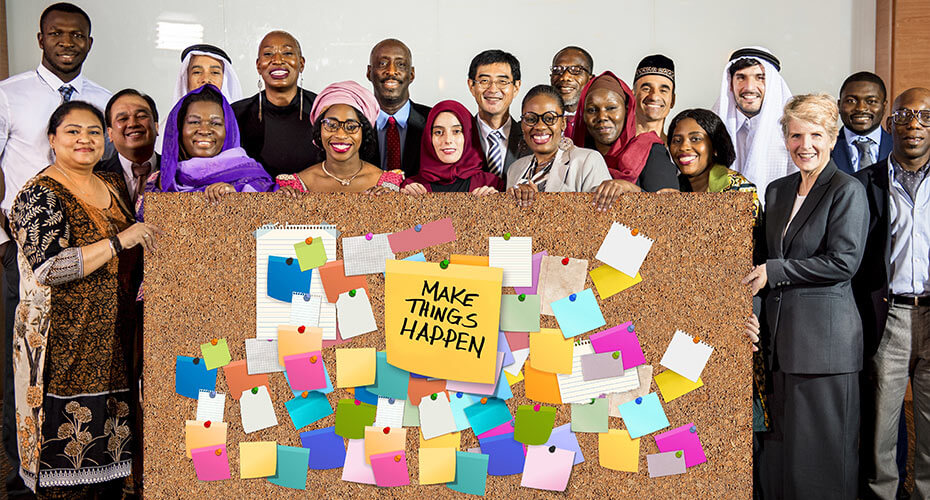 Eine Gruppe von Menschen unterschiedlicher Herkunft steht hinter einer Pinwand, auf der zu lesen ist: Make things happen.