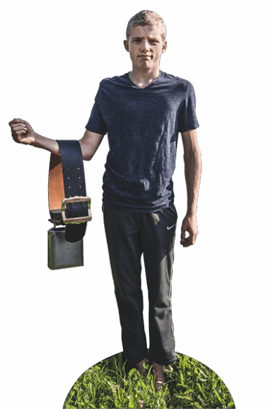 Ein junger Bergbauer aus der Schweiz steht auf der Weide und zeigt eine Kuhglocke.